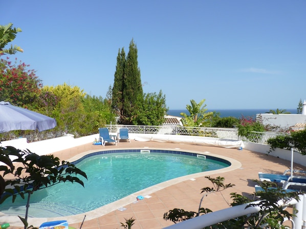 Una piscina de borde curvo, rodeada de sillones de descanso y una valla blanca.