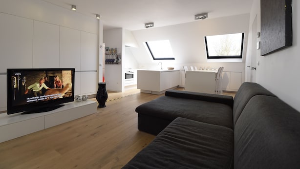 A modern living room with a flat-screen TV, a grey sofa, and a kitchen in the background. - 2 Bedroom apartment near center Ghent (Gent)