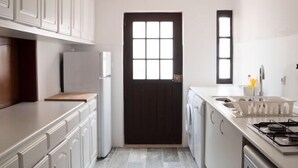Une cuisine compacte avec des meubles blancs, une porte noire, une fenêtre, ainsi qu’un lave-linge et un sèche-linge intégrés.