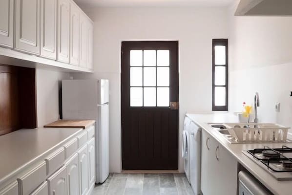 A compact kitchen with white cabinetry, a black door, a window, and a built-in washer and dryer.