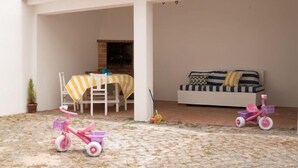 Un patio couvert avec une table et des chaises, un canapé et deux tricycles pour enfants.