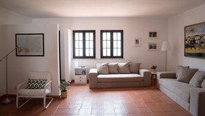 Un salon avec deux canapés, un fauteuil à bascule, une petite table avec une lampe et une fenêtre avec des stores.