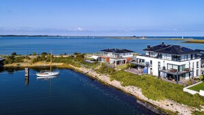 Een pand aan het water met moderne huizen, een steiger en uitzicht op de zee en het land in de verte.