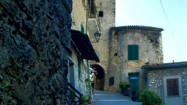 A narrow street with stone buildings, a clock tower, and a clear sky. - Typical home country quaint with antique furniture (cineto romano)