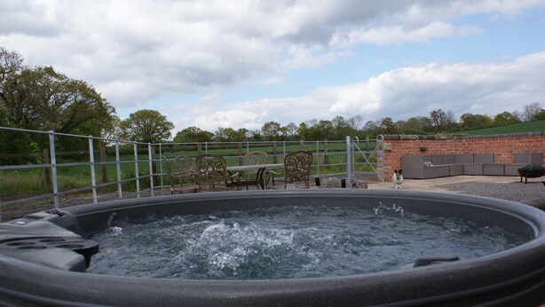 A hot tub with a wooden frame, surrounded by a metal fence and a brick wall. - Granary at Oaks Barn Farm, Kadai fire bowl & optional hot tub, country location (Alcester)