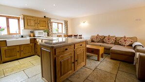 A modern kitchen with wooden cabinets, a central island, and a dining area with a sofa and table. - Granary at Oaks Barn Farm, Kadai fire bowl & optional hot tub, country location (Alcester)