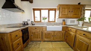 A kitchen with wooden cabinets, a built-in oven, a sink, and a window with flowers. - Granary at Oaks Barn Farm, Kadai fire bowl & optional hot tub, country location (Alcester)
