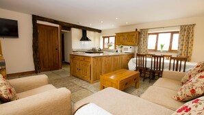 A spacious living area with a wooden sofa set, a wooden coffee table, and a dining area with wooden chairs and a table. - Granary at Oaks Barn Farm, Kadai fire bowl & optional hot tub, country location (Alcester)