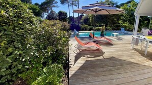 Eine Holzterrasse mit Pool, Liegestühlen und Sonnenschirm.