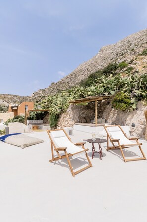 Eine Dachterrasse mit weißen Liegestühlen, einem kleinen Tisch und einer Pergola.