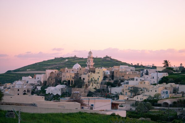 A coastal town with historic architecture, including a prominent church with a dome and bell tower, set against a backdrop of hills and a sunset sky.