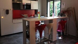 A modern kitchen with a central island, red bar stools, and a window with a view of greenery. - Beautiful T3 "design", 4 *, quiet in the garden, town center -2 bedrooms, 2/5 people (Lourdes)