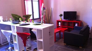 A modern living room with a dining area, a red TV stand, and a sofa. - Beautiful T3 "design", 4 *, quiet in the garden, town center -2 bedrooms, 2/5 people (Lourdes)