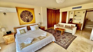 Una camera d'albergo con un letto grande, una zona salotto con divano e tavolino, armadietti in legno e un ampio specchio a parete.