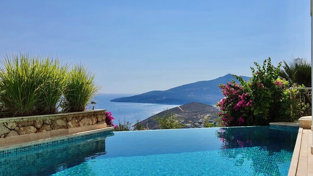 Una piscina a sfioro con acqua cristallina, circondata da mura in pietra e rigogliosa vegetazione, affacciata su un paesaggio costiero panoramico.