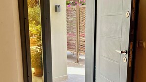 Ingresso di un hotel con porta in vetro che dà su uno spazio esterno coperto, decorato con piante in vaso e una struttura a grigliato.