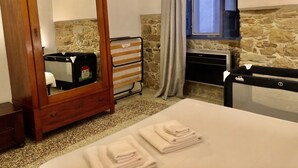 A bedroom with a wooden wardrobe, a bed with folded towels, a radiator, and a stone wall.