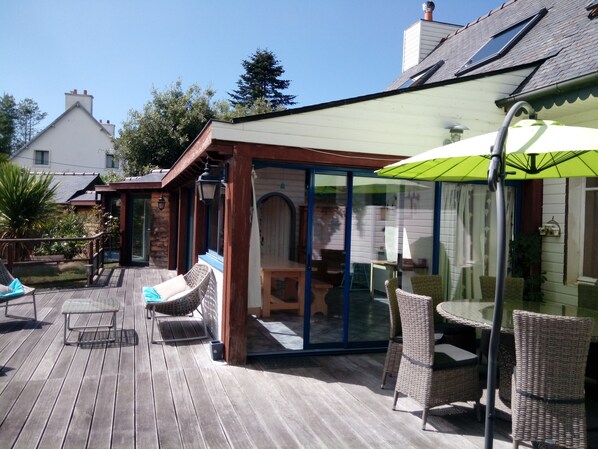 A wooden deck with wicker furniture, a glass enclosure, and a green umbrella.