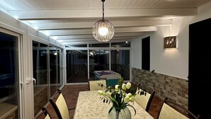 Zona pranzo con un tavolo grande, sedie, un vaso con fiori, un lampadario e vista su piscina e area esterna.
