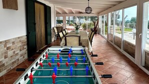 Un'ampia area interna con un tavolo da calcio, un tavolo da pranzo con sedie e ampie finestre che offrono vista sull'esterno.