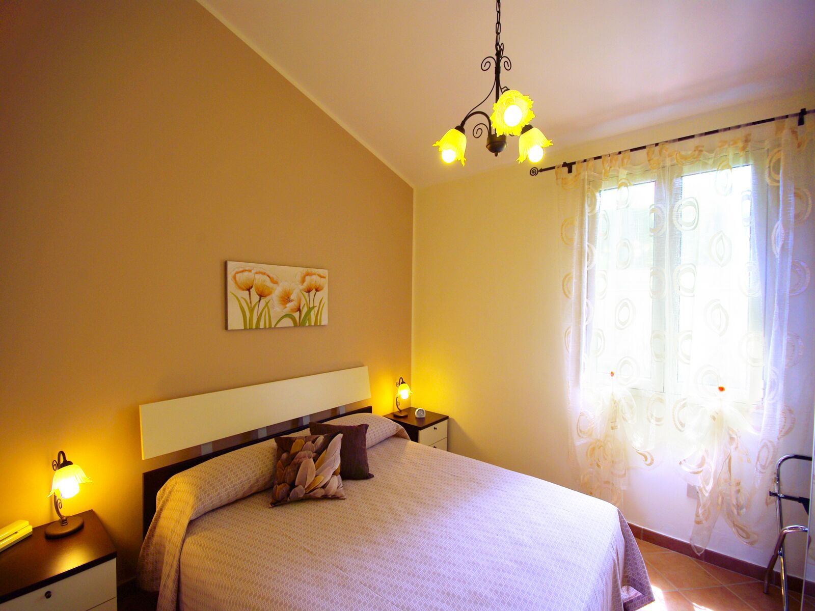 A bedroom with a bed, bedside lamps, a painting on the wall, and a window with curtains.