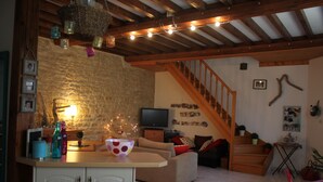 Un salon chaleureux avec un mur en pierre, des poutres apparentes, un canapé, un téléviseur et un escalier.