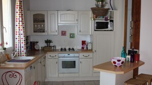 Une cuisine avec des meubles blancs, un plafond en bois, une chaise rouge, une table en bois et un four à micro-ondes.
