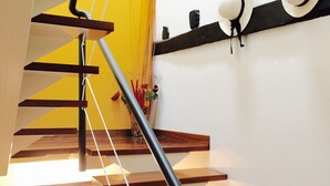Una escalera con barandilla negra, escalones de madera y una pared amarilla con un cuadro enmarcado.