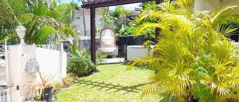 Un jardin bien entretenu, agrémenté d’une pergola, de palmiers et d’une statue.