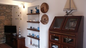 Ein Wohnzimmer mit Steinwand, Holzböden, offenen Regalen mit Dekoration, einem Fernseher und einem Holzschrank mit Glastüren.