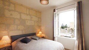 Quarto com cama, duas luminárias de cabeceira, janela com cortinas e vista para um pátio.