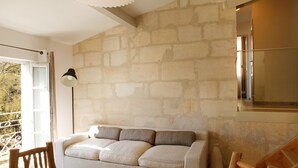 Uma sala de estar acolhedora com parede de pedra, um sofá branco, uma cadeira de madeira e um abajur.