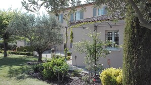 Un bâtiment avec un toit en tuiles, un jardin avec différentes plantes et un arbre au premier plan.