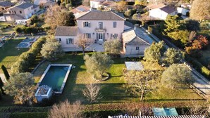 Une vue aérienne d’une grande maison à deux étages, dotée d’une piscine et entourée d’une pelouse bien entretenue et d’arbres.
