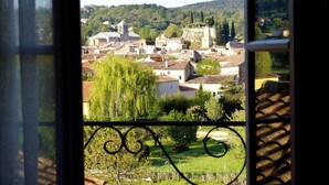Une vue à travers une fenêtre sur une ville, avec des bâtiments, de la verdure et une colline en arrière-plan.