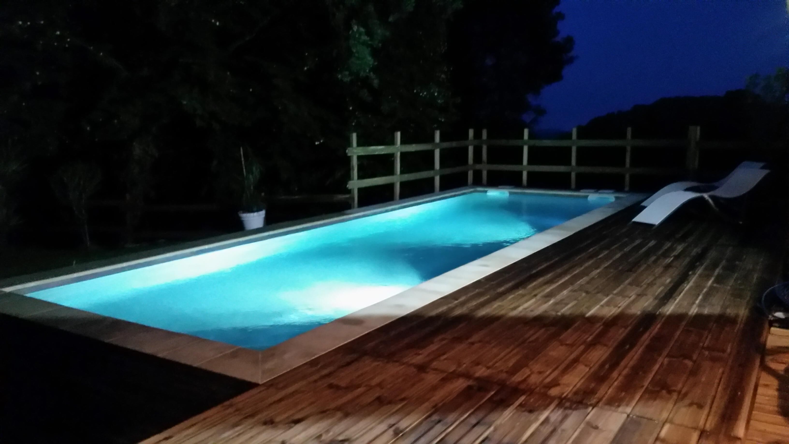 Una piscina rectangular con cubierta de madera, rodeada por una valla de madera y árboles.