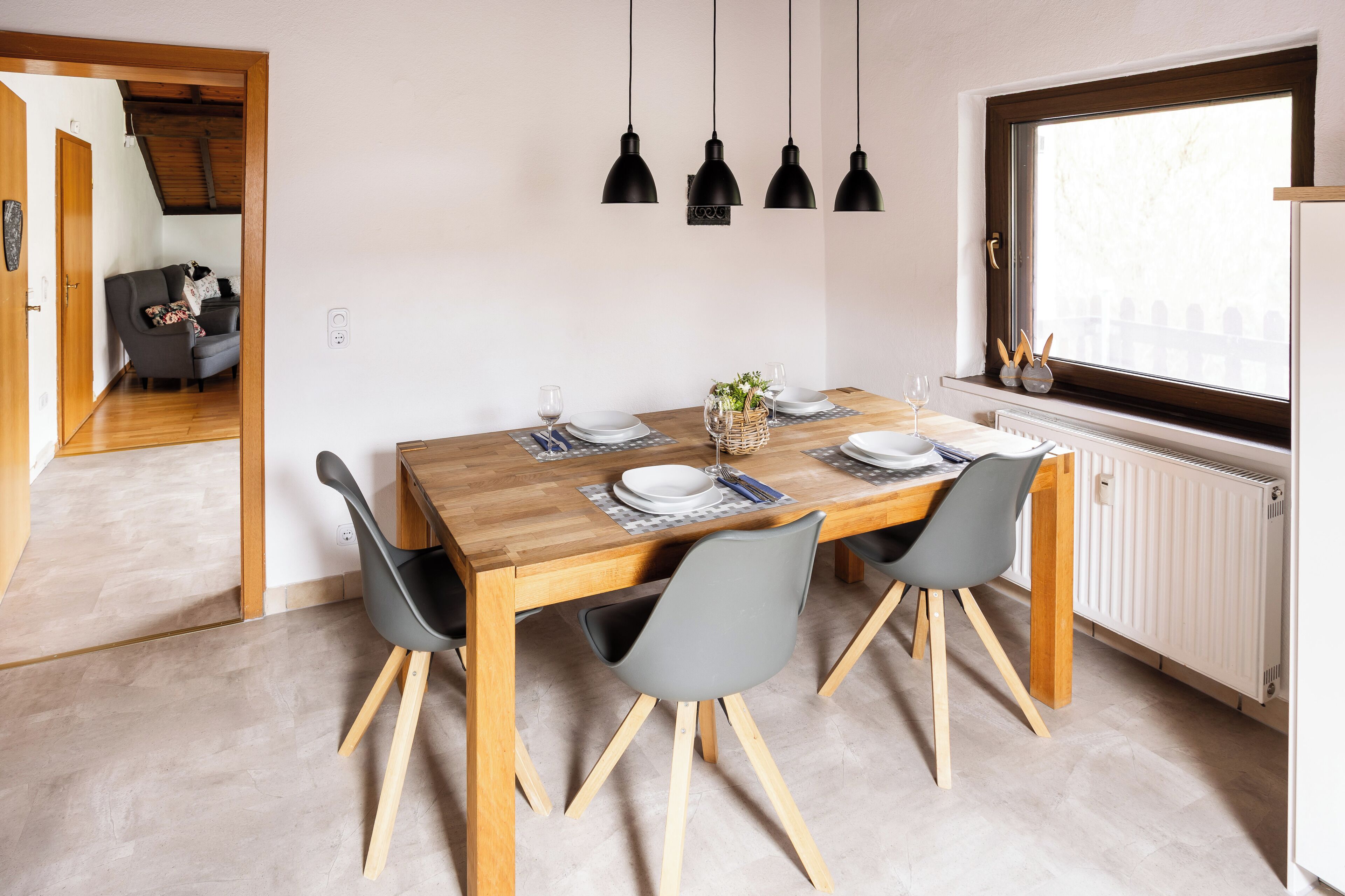 Ein Essbereich mit einem Holztisch, vier grauen Stühlen und schwarzen Pendelleuchten.