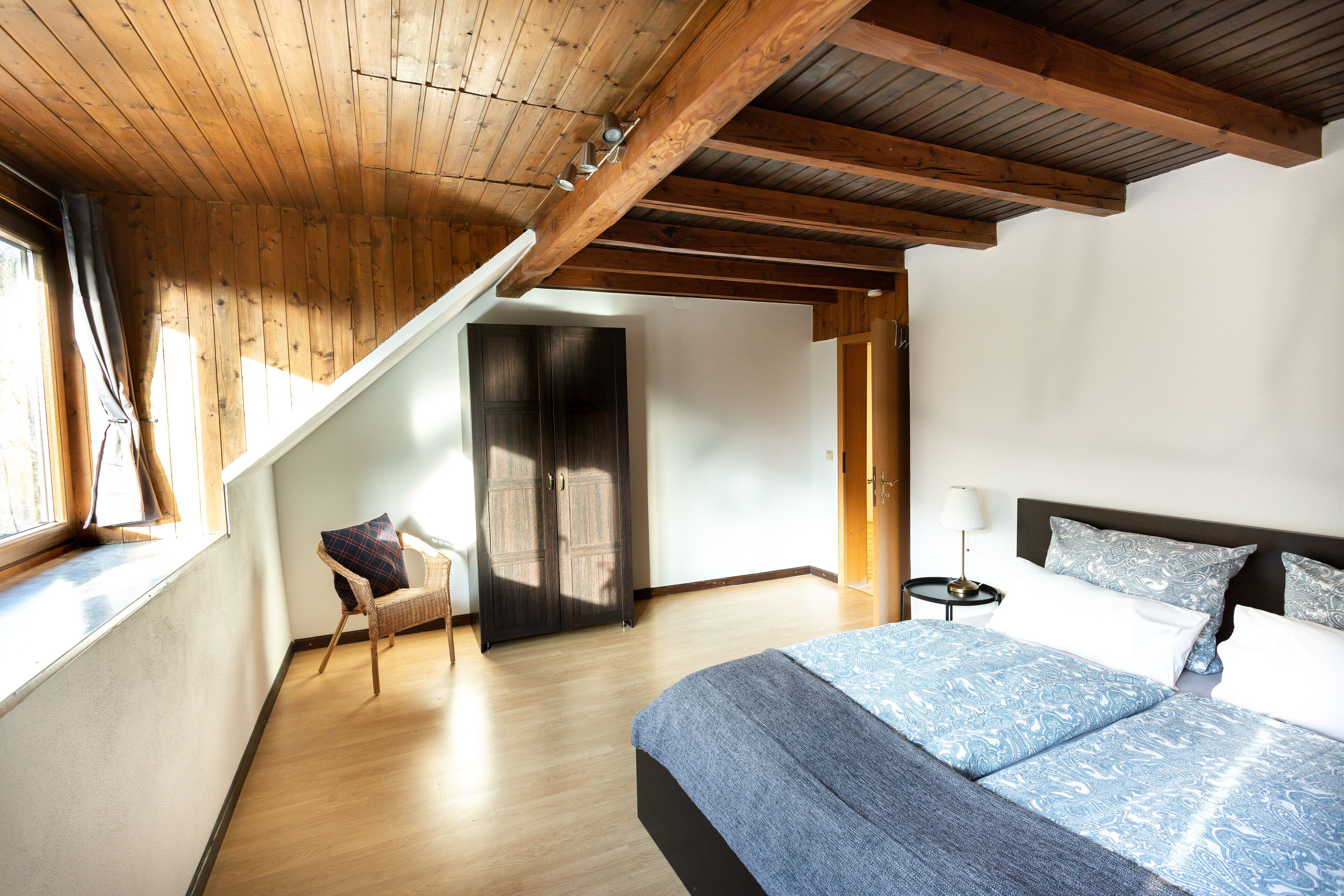 Une chambre avec un plafond en bois, un grand lit avec une literie à motifs, une chaise et une armoire.