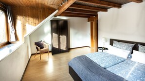 A bedroom with a wooden ceiling, a large bed with patterned bedding, a chair, and a wardrobe. - Country Living in the southern Eifel, vacation apartment in the Sauertal N° 2 (Ralingen)