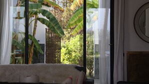 Une pièce avec une grande fenêtre, un tapis blanc et moelleux, et un miroir rond accroché au mur.