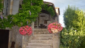 A stone staircase leading to a rustic building with a wooden door and a small table with chairs outside.