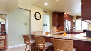 A kitchen with a central island, bar stools, a clock, and a refrigerator. - Partial Ocean Views, Top Floor. Beach Gear Included.  Vista Waikoloa A304 (Waikoloa Beach Resort)