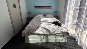 A bedroom with a bed, two bedside tables, a door, a window with curtains, and a painting on the wall.