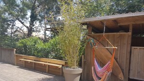 A wooden deck with a hammock, a planter with bamboo, and a wooden structure.