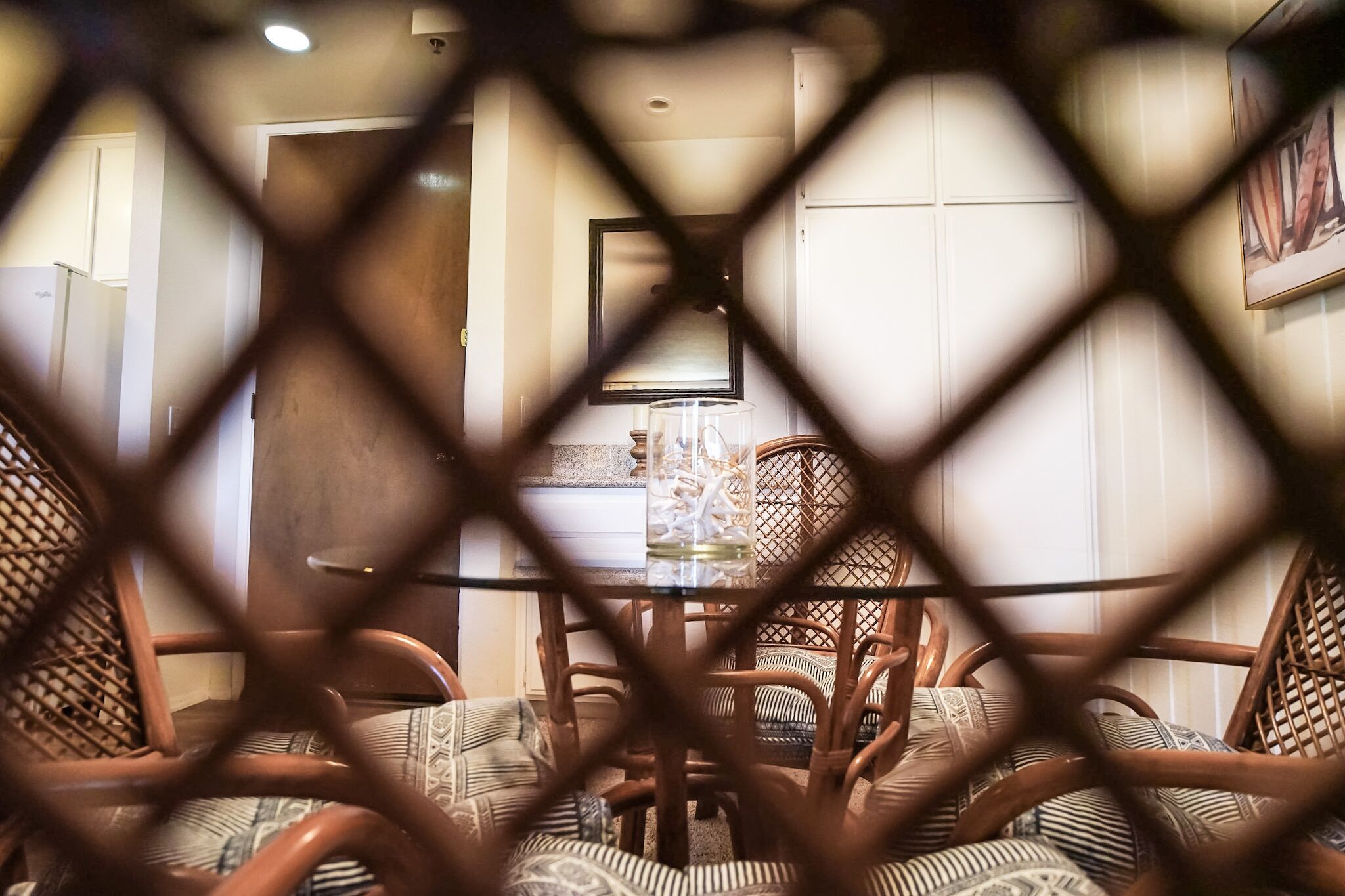 Una habitación con una mesa de comedor rodeada de sillas de mimbre, una mesa con cubierta de vidrio y una puerta al fondo.