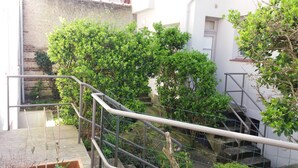 Una escalera con barandillas de metal, rodeada de exuberante follaje verde y un muro de ladrillo.