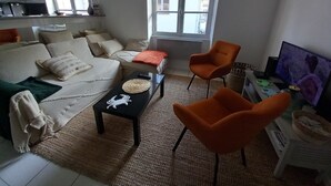 Una sala de estar con un sofá, dos sillones naranjas, una mesa de centro y un televisor.