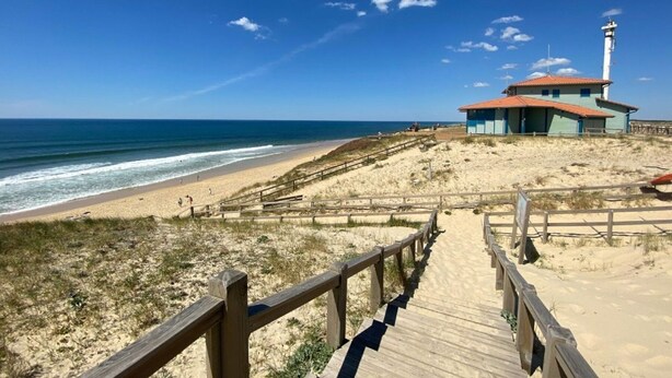 Ein Strand mit einer Holzpromenade, die zu einem Gebäude mit einem Leuchtturm führt.