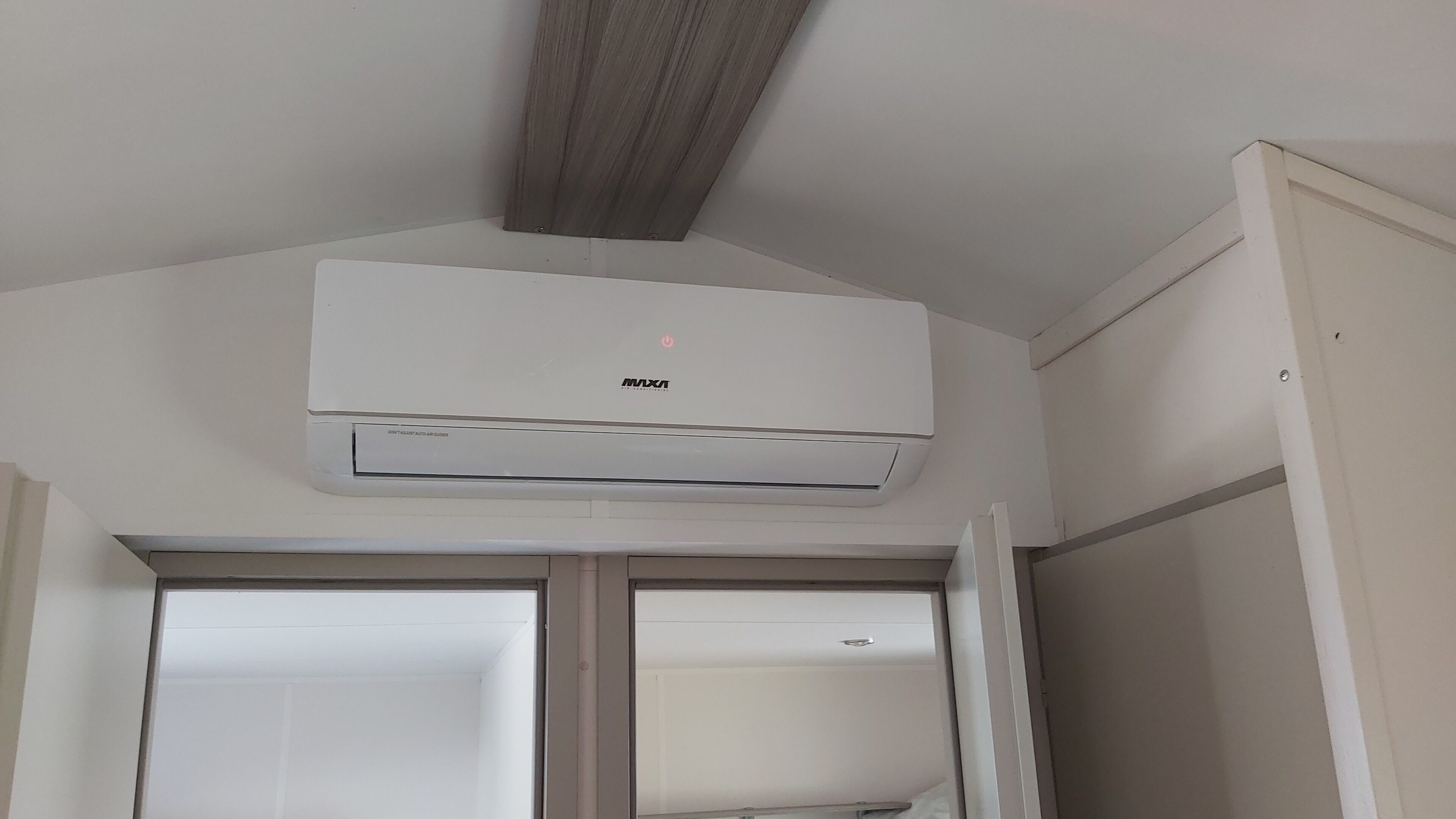 Eine weiße Klimaanlage, die an einer Decke befestigt ist, unter der ein Holzbalken verläuft.