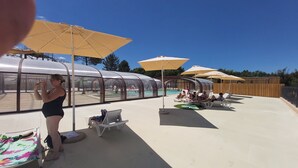 Ein Poolbereich mit Sonnenschirmen, Liegestühlen und einem überdachten Schwimmbecken.
